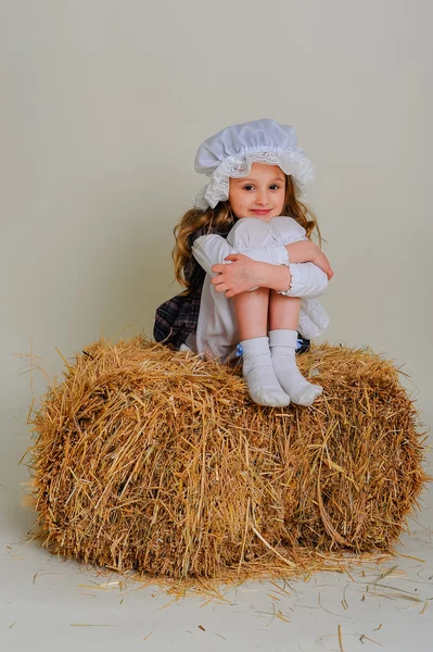 Girl in dress sitting on a rustic vintage straw bale. — Stock Photo, Image