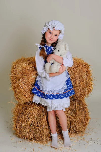 Girl in dress standing near a rustic vintage hay with a toy. — Stock Photo, Image