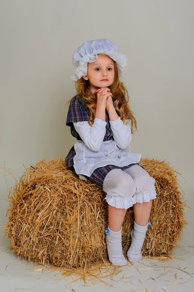 Girl in dress sitting on a rustic vintage straw bale. — Stock Photo, Image