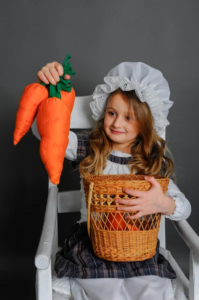 Fille avec un panier et des carottes sur un fond gris — Photo