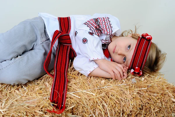 Ukrainian girl in national dress and jeans lying in the manger. — Stock Photo, Image