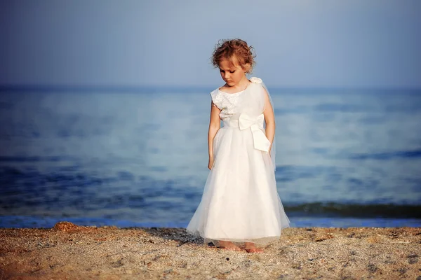 Menina em um vestido branco caminha na praia — Fotografia de Stock