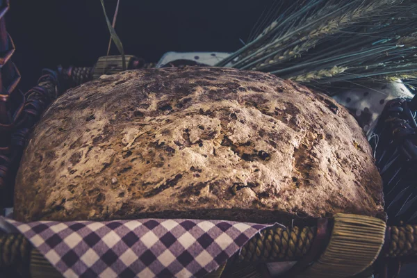 Estilo vintage: artesanato de pão caseiro sem glúten e sem fermento close-up em cesta de vime com orelhas de cevada embrulhadas em um guardanapo xadrez — Fotografia de Stock