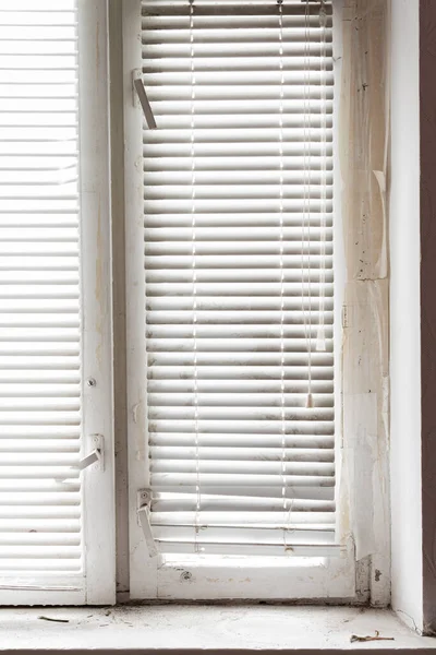 Wooden window and white horizontal blinds. A fragment of an old wooden window and a dirty old window sill.