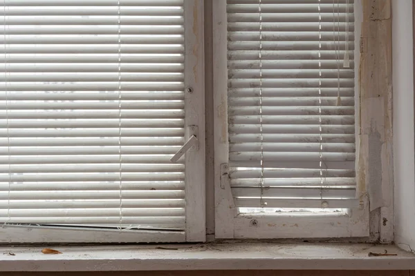 Wooden window and white horizontal blinds. A fragment of an old wooden window and a dirty old window sill.