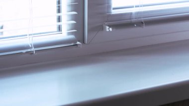 Kadının eli pencere pervazındaki döküntüleri kaldırıyor ve pencere pervazındaki tozları sarı bir paçavrayla siliyor..