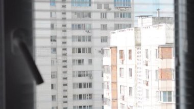 Pencerenin perdelerinden bina manzarası var. Kadın eli perdeleri açtı, pencere pencereden dışarı baktı ve perdeleri kapattı..