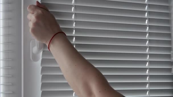 Μια γυναίκα ανοίγει λευκό πλαστικό παράθυρο από τη λαβή και κλείστε τα blinds. — Αρχείο Βίντεο