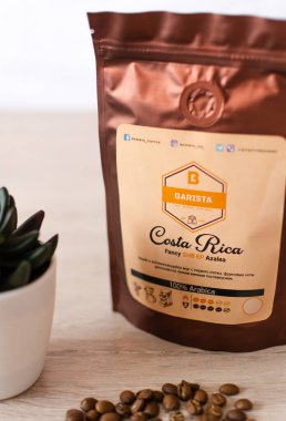 Tiraspol, Moldova - 19 Mart 2021: Deodorant kapaklı yumuşak ambalajlı kahve. Kosta Rika kahvesi,% 100 Arap kahvesi, kahve markası ve beyaz tencerede dekoratif yeşil çiçek. 45 derece açıyla.