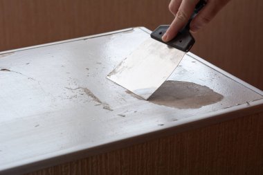 An anonymous person removes a layer of old paint with a spatula clipart