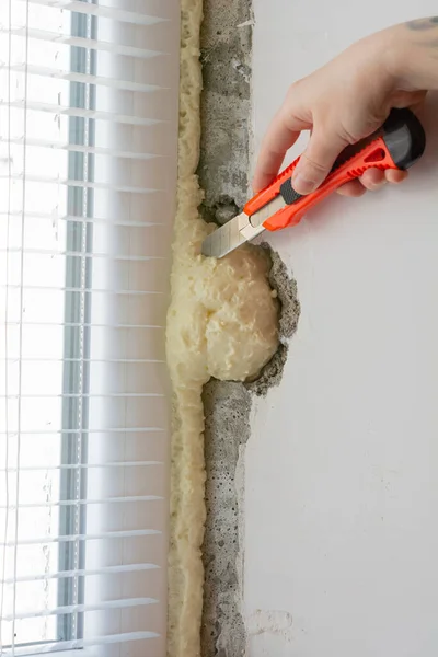 An anonymous person cuts polyurethane foam with a construction knife. Installation of windows. Polyurethane foam on the slope of the window. Sealing window slopes.