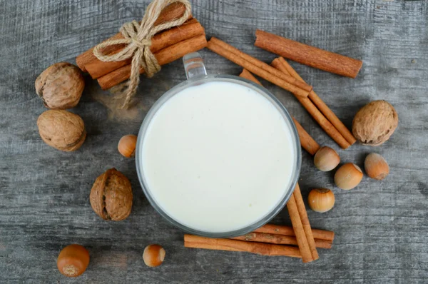 Tazza di latte caldo con cannella, spezie e nocciole, noci, primo piano su fondo di legno — Foto Stock