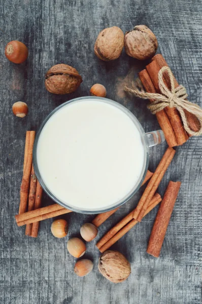 Secangkir susu panas dengan kayu manis, rempah-rempah dan hazelnut, kenari, penutup di latar belakang kayu — Stok Foto