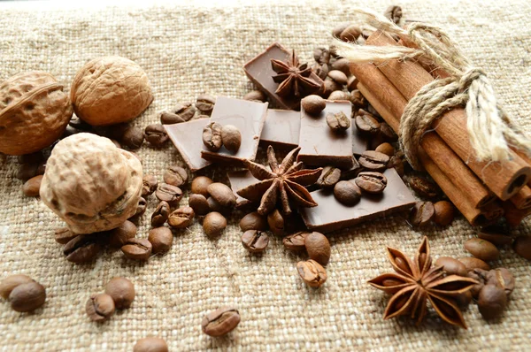Fahéj, kávé, csokoládé, szegfűszeg, mogyoró dió a zsákolás a háttérben — Stock Fotó