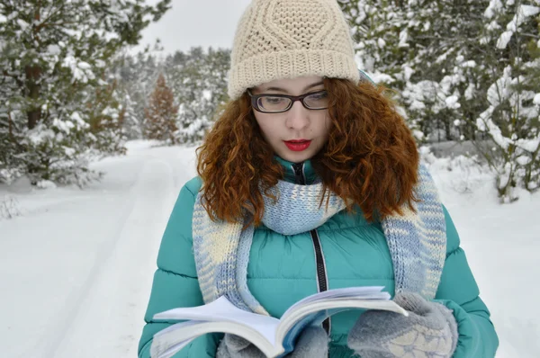 Krásná, mladá, kudrnaté děvče, oblečené v bundě, pletené čepice, Pletené šály, čtení zamyšleně kniha v parku — Stock fotografie