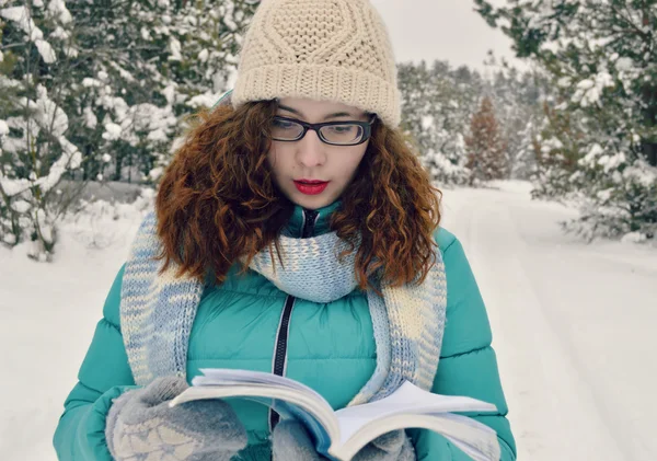 Krásná, mladá, kudrnaté děvče, oblečené v bundě, pletené čepice, Pletené šály, čtení zamyšleně kniha v parku — Stock fotografie