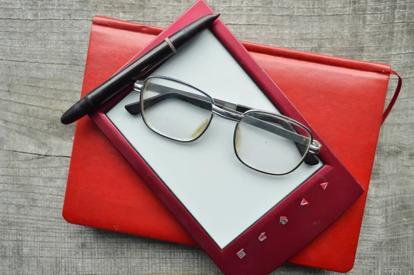 E-book rouge, Bloc-notes, lunettes de lecture, tasse de café chaude sur fond en bois — Photo