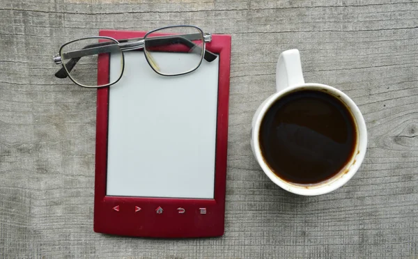 Libro elettronico rosso, Blocco note, occhiali da lettura, tazza di caffè caldo su sfondo di legno — Foto Stock