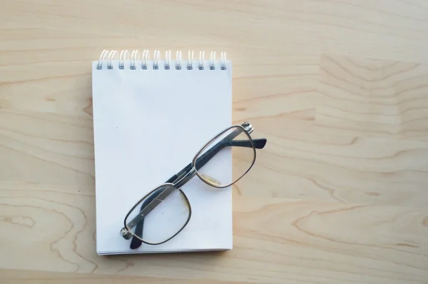 Cuaderno de notas, vasos de lectura, taza de café caliente sobre fondo de madera . — Foto de Stock