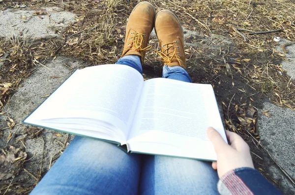 Mädchen in braunen Stiefeln liest im Park ein faszinierendes Buch — Stockfoto