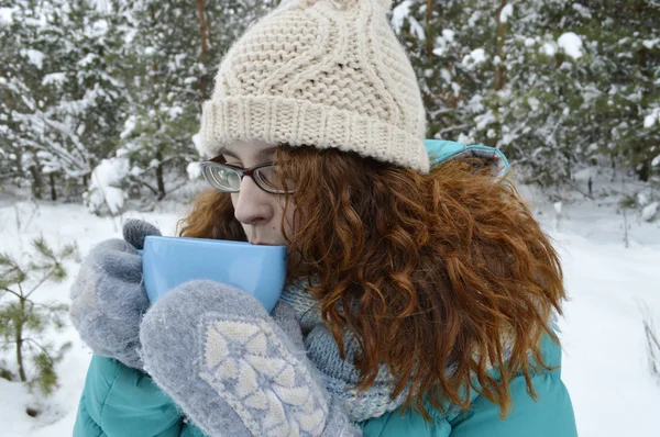 Chica de cabello oscuro vestida con una chaqueta turquesa, sombrero de lana corporal, y una bufanda azul claro, leyendo un libro en el Parque, bebiendo té, café, cacao —  Fotos de Stock