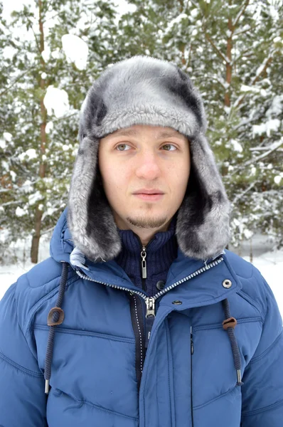 En ung, mörkhårig man, varmt klädd, stående i en snöig skog — Stockfoto