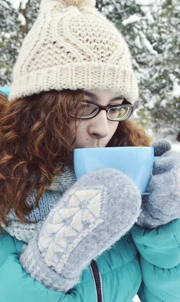 Chica de cabello oscuro vestida con una chaqueta turquesa, sombrero de lana corporal, y una bufanda azul claro, leyendo un libro en el Parque, bebiendo té, café, cacao —  Fotos de Stock