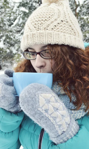 Chica de cabello oscuro vestida con una chaqueta turquesa, sombrero de lana corporal, y una bufanda azul claro, leyendo un libro en el Parque, bebiendo té, café, cacao —  Fotos de Stock