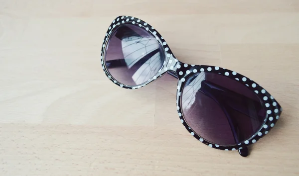 Black and white sunglasses with violet lenses on a wooden table closeup — Stock Photo, Image
