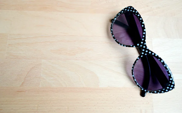 Black and white sunglasses with violet lenses on a wooden table closeup — Stock Photo, Image