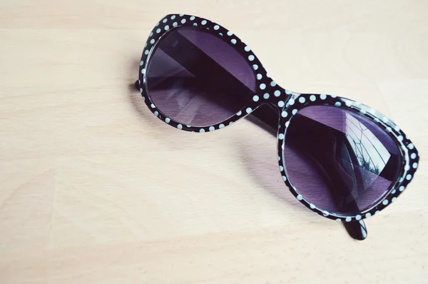 Lunettes de soleil noires et blanches avec lentilles violettes sur une table en bois gros plan — Photo