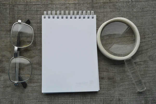 Journal, notes, bloc-notes, stylo, crayon, lunettes, loupe sur fond bois — Photo