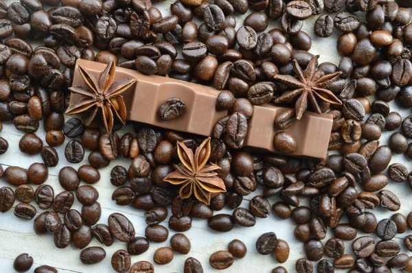 Barre de chocolat noir, barre de chocolat au lait, grains de café, anis étoilé, bâtonnets de cannelle, assaisonnements, épices, gros plan sur un fond en bois blanc — Photo