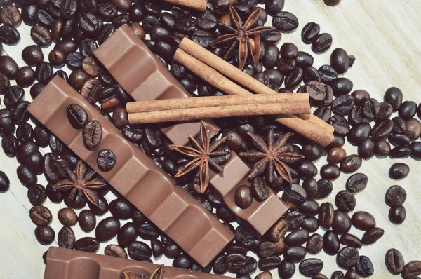 Barre de chocolat noir, barre de chocolat au lait, grains de café, anis étoilé, bâtonnets de cannelle, assaisonnements, épices, gros plan sur un fond en bois blanc — Photo