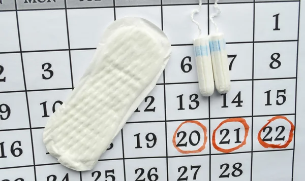 Женская гигиена, календарь макро-менструаций с тампонами из хлопка, оранжевый Гербер, прокладки на красном фоне — стоковое фото
