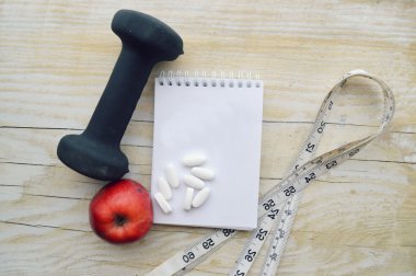 Dumbell with measuring tape and apple with pills and note pad clipart