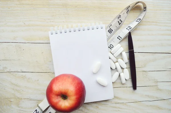 Maßband und Apfel mit Pillen und Notizblock — Stockfoto