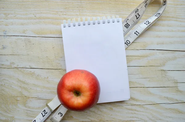 Notepad with measuring tape and apple — Stock Photo, Image