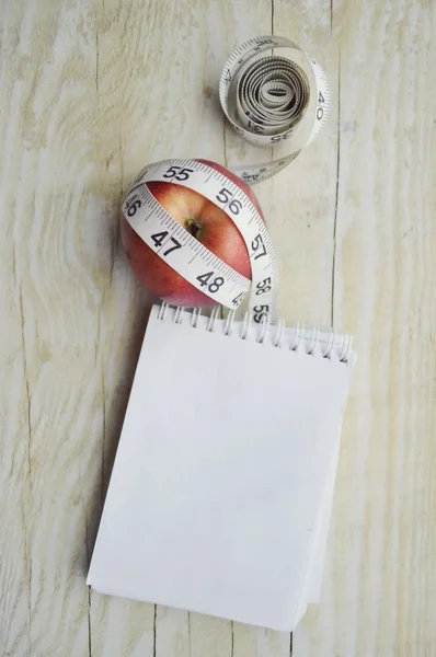 Cuaderno con cinta métrica y una manzana —  Fotos de Stock