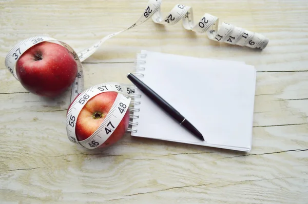 Notebook with measuring tape and two apples