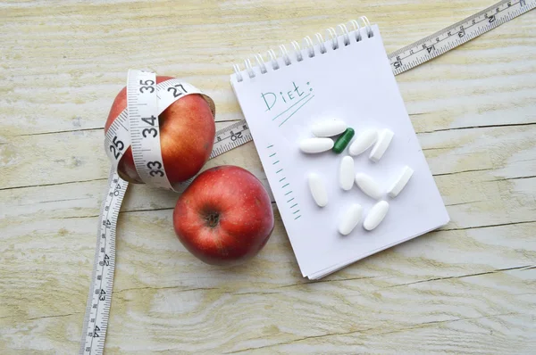 Two apples, measuring tape, pills and notebook