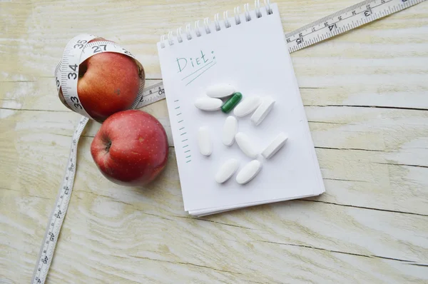 Two apples, measuring tape, pills and notebook — Stock Photo, Image