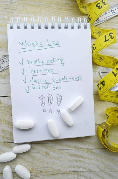 Caderno com plano de dieta e uma fita métrica com pílulas — Fotografia de Stock
