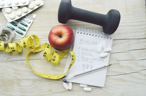 Cinta métrica, pastillas, manzana y cuaderno con mancuerna — Foto de Stock