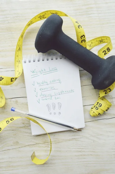 Measuring tape, notebook and dumbbell — Stock Photo, Image