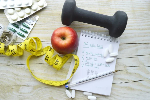 Ruban à mesurer, cahier et haltère avec pilules et pomme — Photo