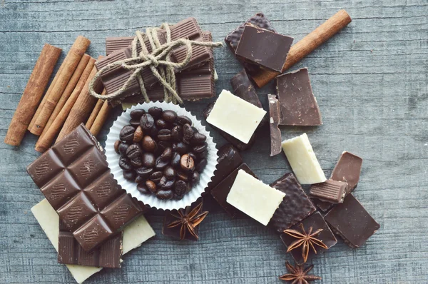 Bar de chocolate, grãos de café, avelãs, nozes, canela, coentro, especiarias. Barra de chocolate, barras de chocolate, diferentes doces de chocolate em um fundo de madeira — Fotografia de Stock