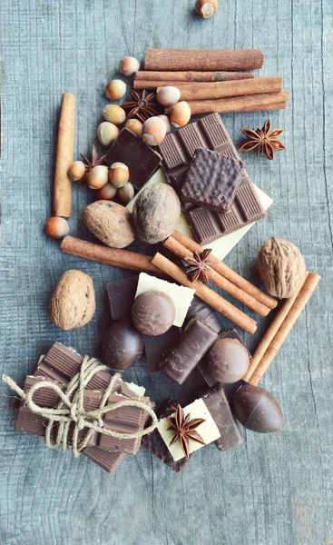 Bar of chocolate, coffee beans, hazelnuts, walnuts, cinnamon, coriander, spices .chocolate bar, candy bars,  different chocolate sweets on a wooden background — Stock Photo, Image