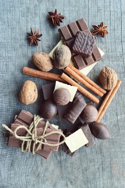 Barretta di cioccolato, chicchi di caffè, nocciole, noci, cannella, coriandolo, spezie. Barretta di cioccolato, barrette di caramelle, diversi dolci al cioccolato su uno sfondo di legno — Foto Stock