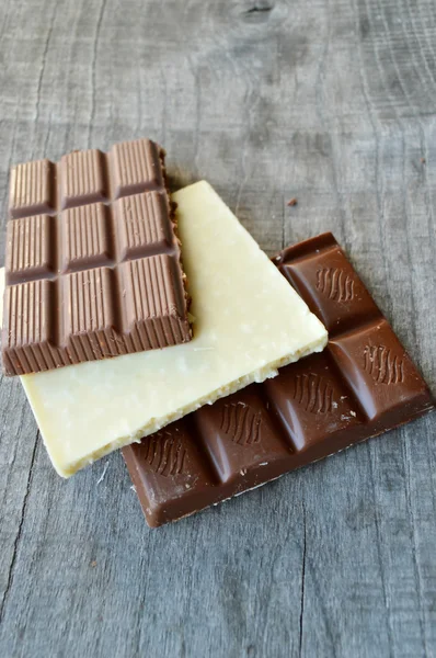 Bar of chocolate, coffee beans, hazelnuts, walnuts, cinnamon, coriander, spices .chocolate bar, candy bars,  different chocolate sweets on a wooden background — Stock Photo, Image